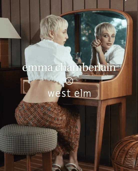 Emma Chamberlain assise devant un miroir de coiffeuse en bois mid-century pour la campagne de collaboration Emma Chamberlain x West Elm