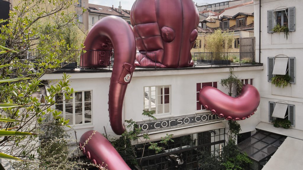 Giant inflatable burgundy sea creature tentacles wrapping around the facade of 10 Corso Como in Milan, each bearing Moncler's signature badge and quilted pocket detailing.