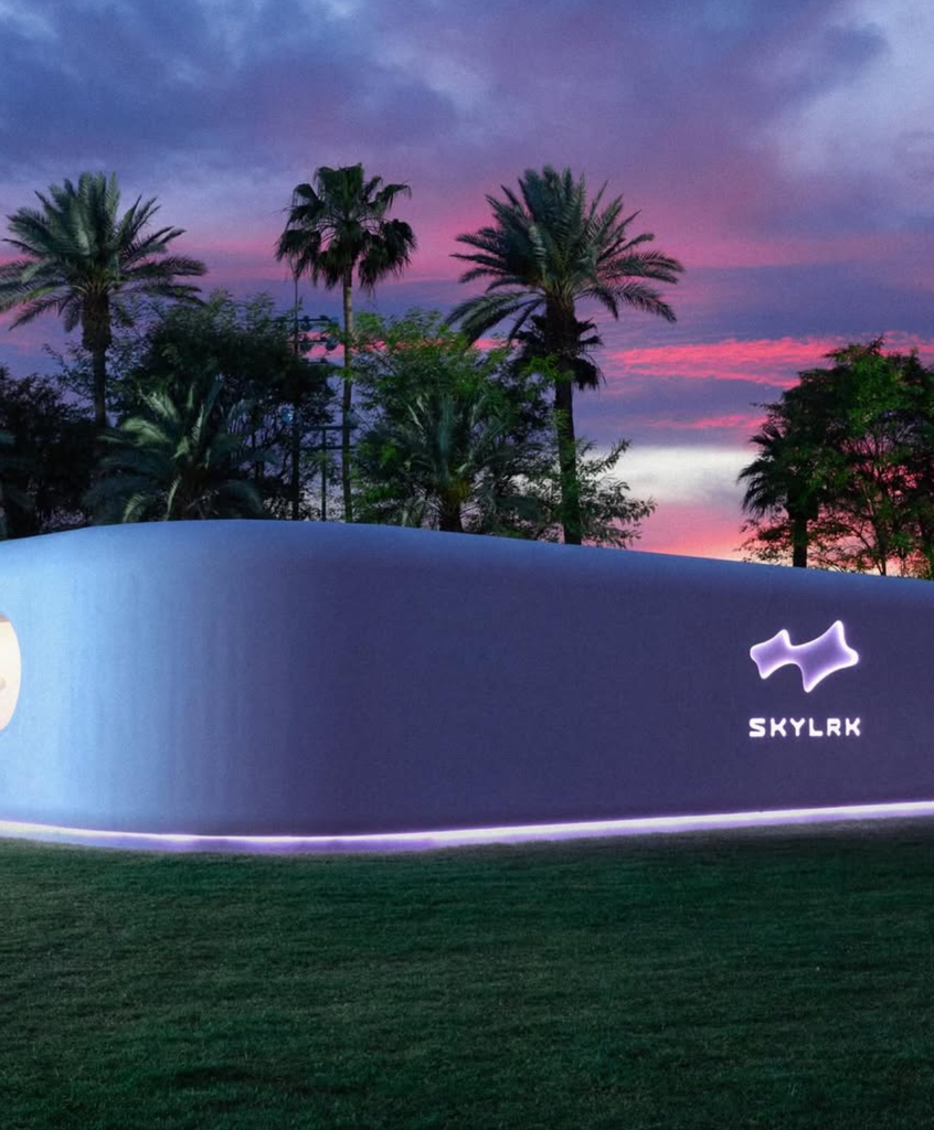A sleek white curved structure glowing with blue LED lighting at dusk, branded with the SKYLRK